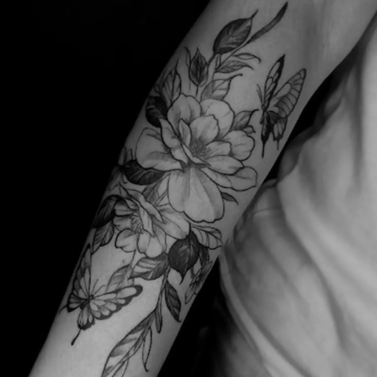 Tatuagem botânica em preto e cinza no braço feita por Egle Justino